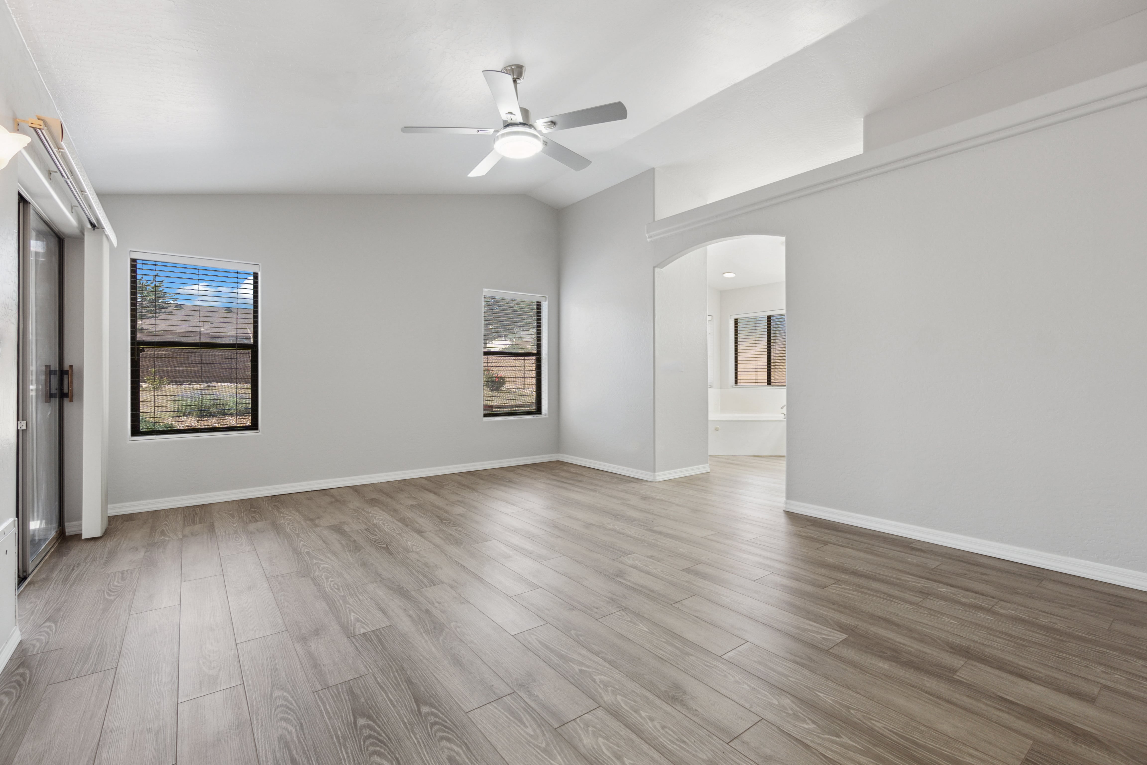 A vacant, well-lit room with wood-style flooring and ceiling fan. Could be used to highlight rental listings, move-in readiness, or staging tips.