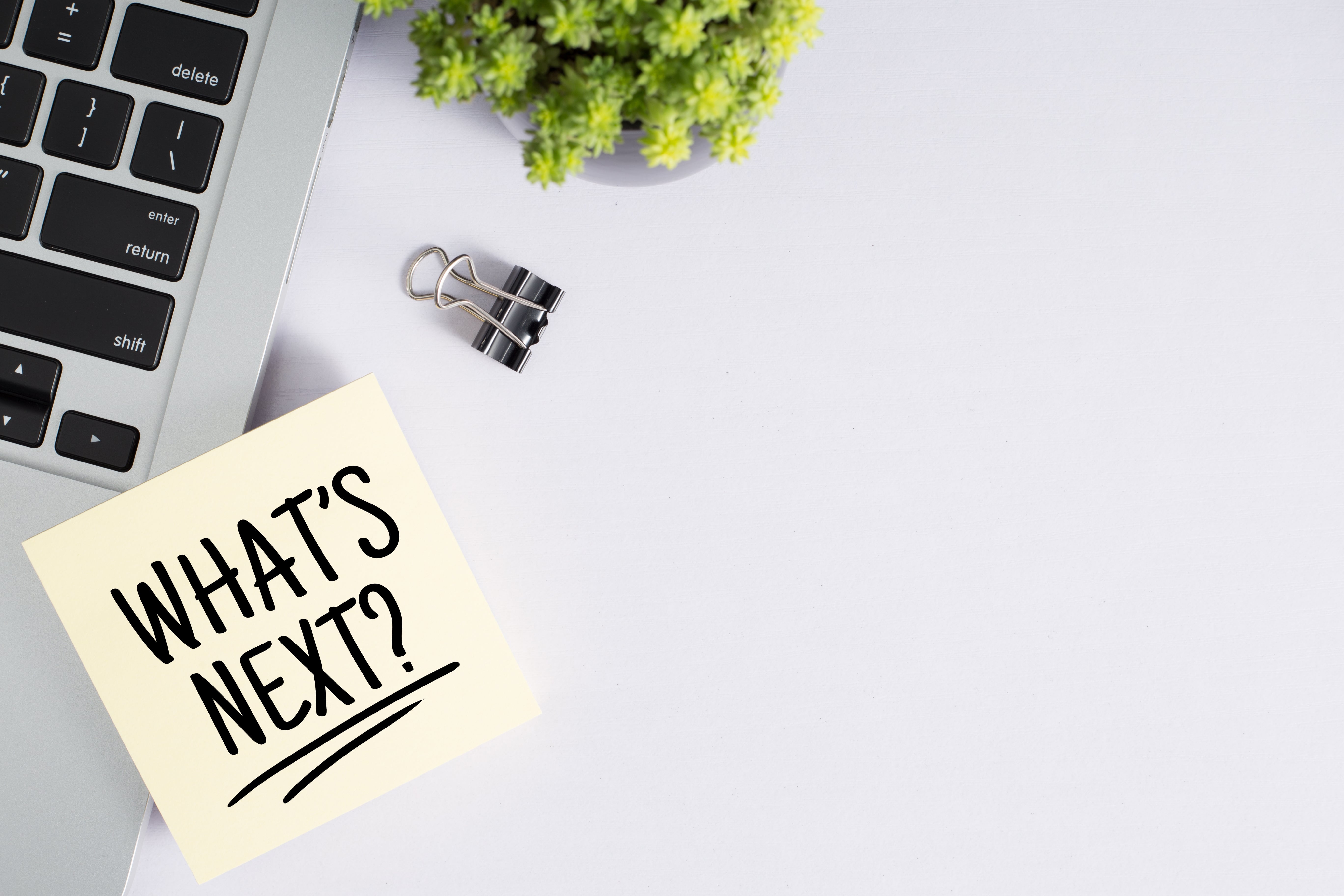 Sticky note reading “What’s Next?” placed beside a laptop keyboard and a small potted plant, symbolizing planning future steps or decisions in a 1031 exchange process.