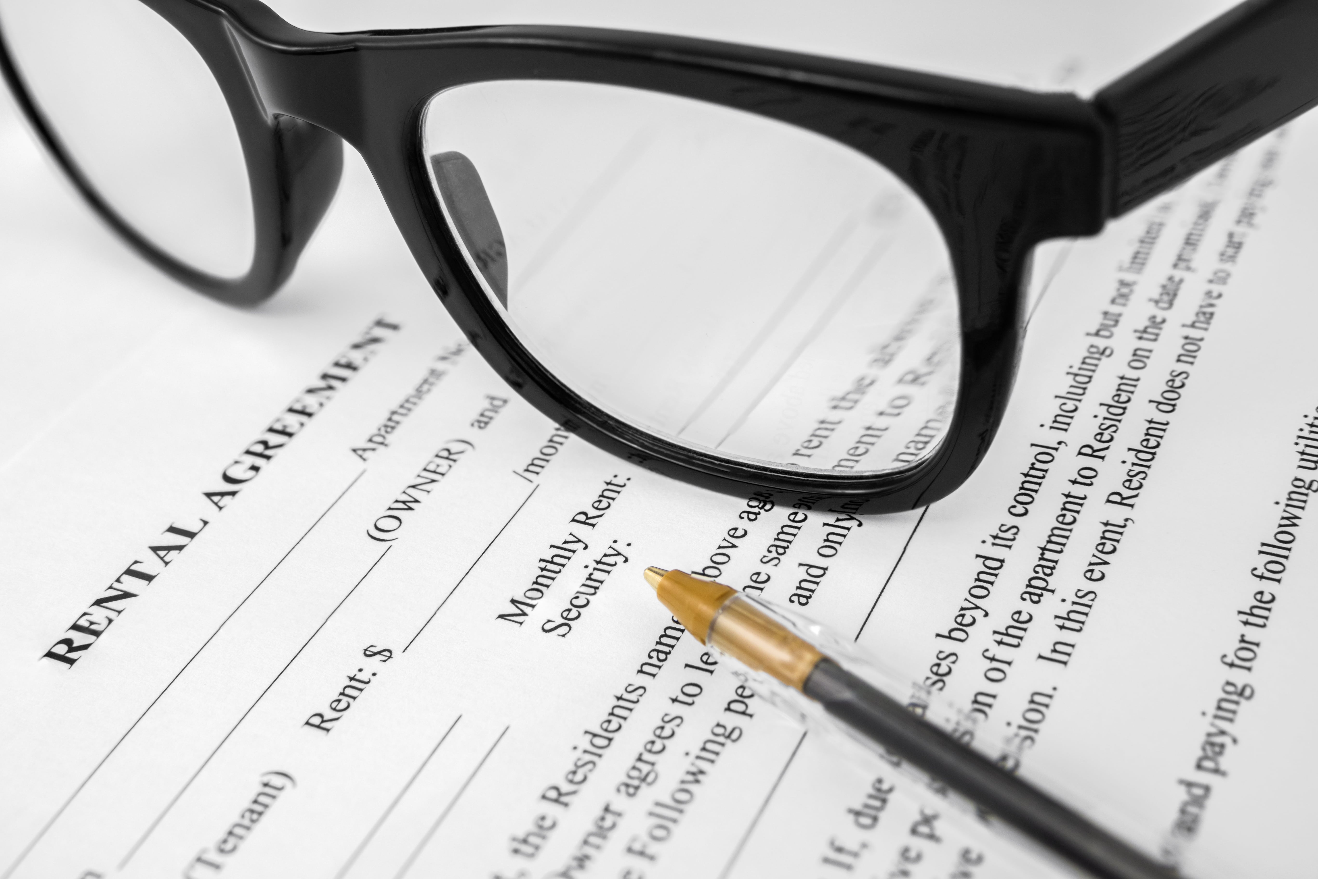 Close-up of a rental agreement document with a pen pointing at the monthly rent section and black eyeglasses resting on the paper.