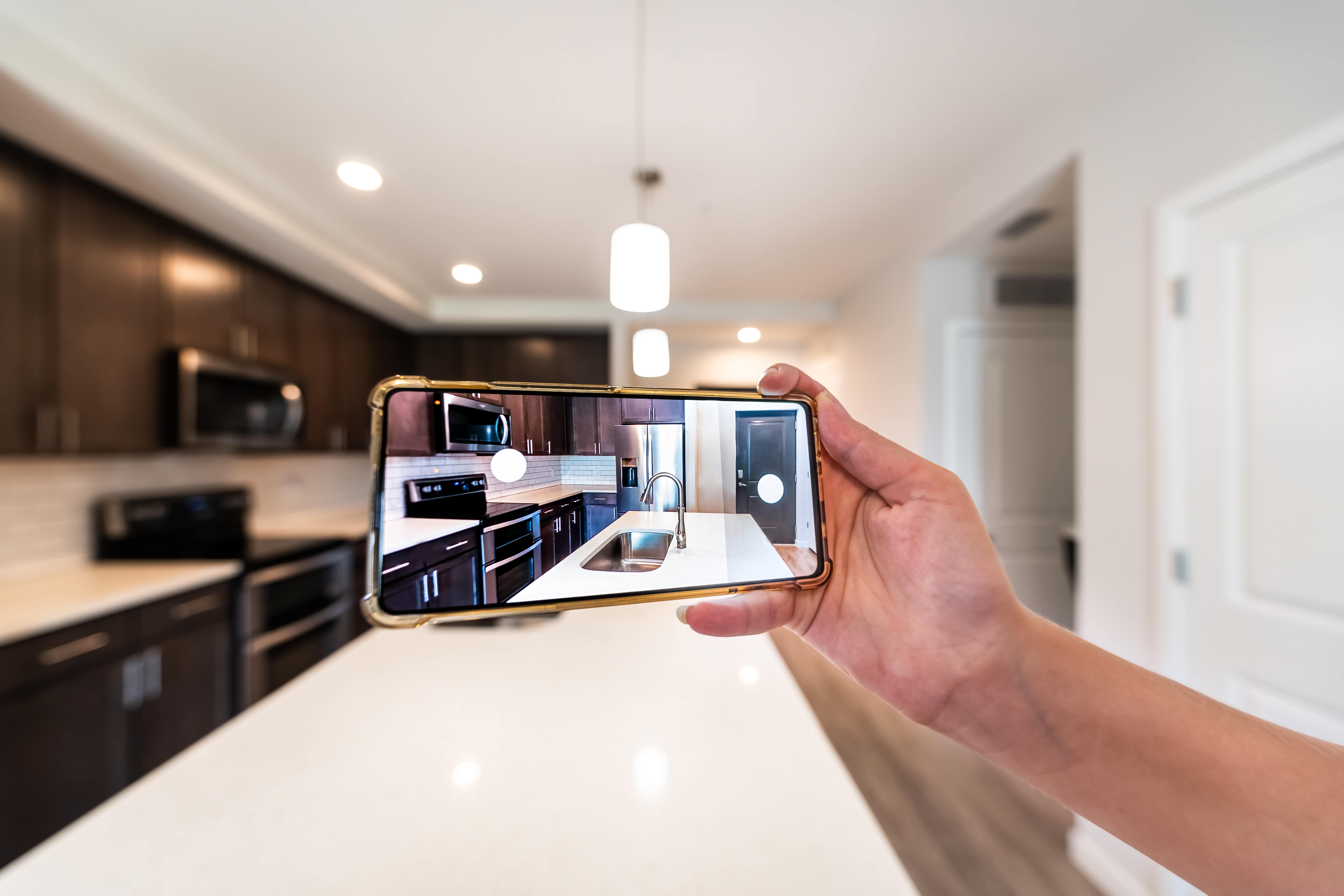 Someone taking a photo or virtual tour of a kitchen with a smartphone. Example of vacant home watch service.