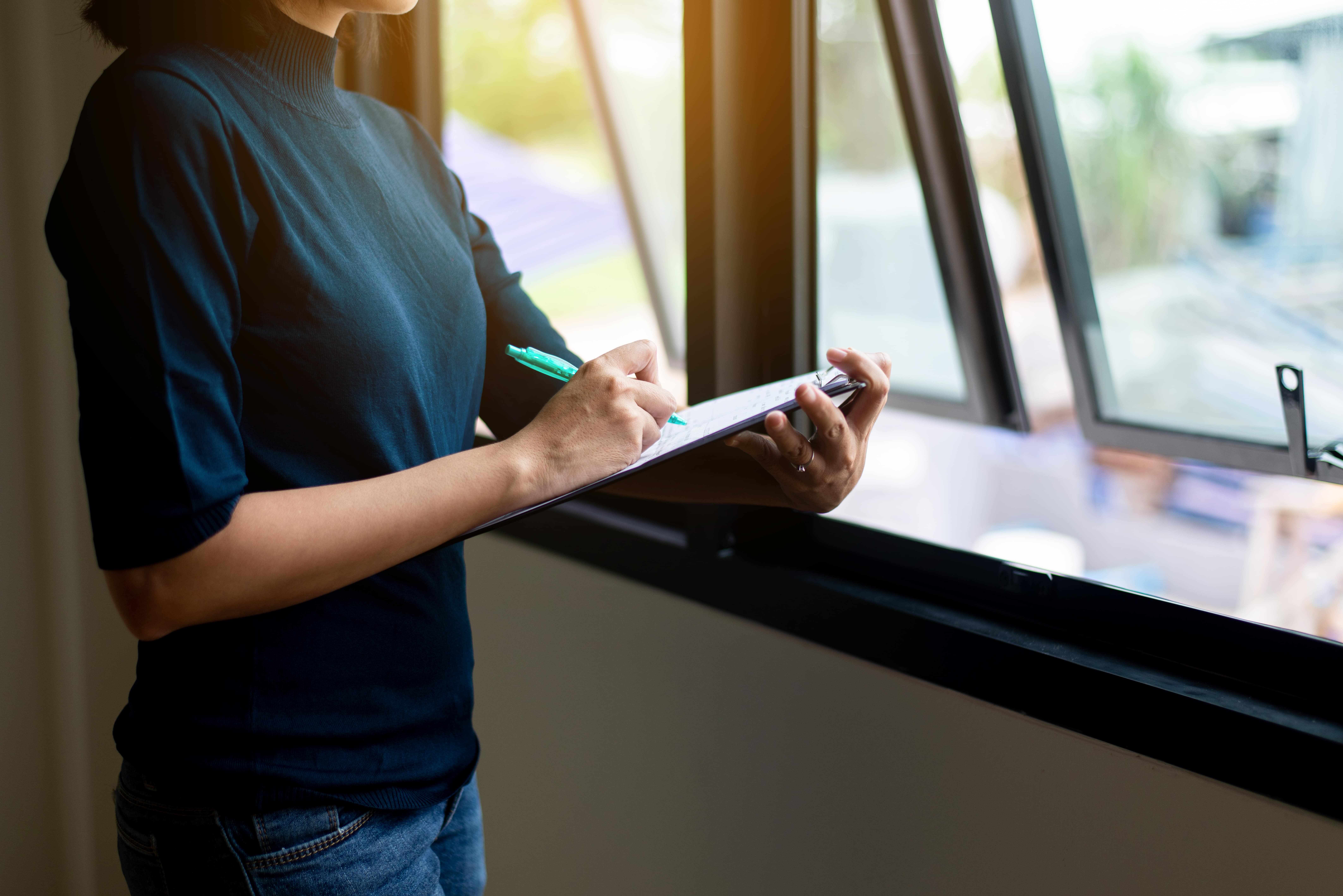 A woman writing on a clipboard near an open window. Good for vacant inspections or documentation.
