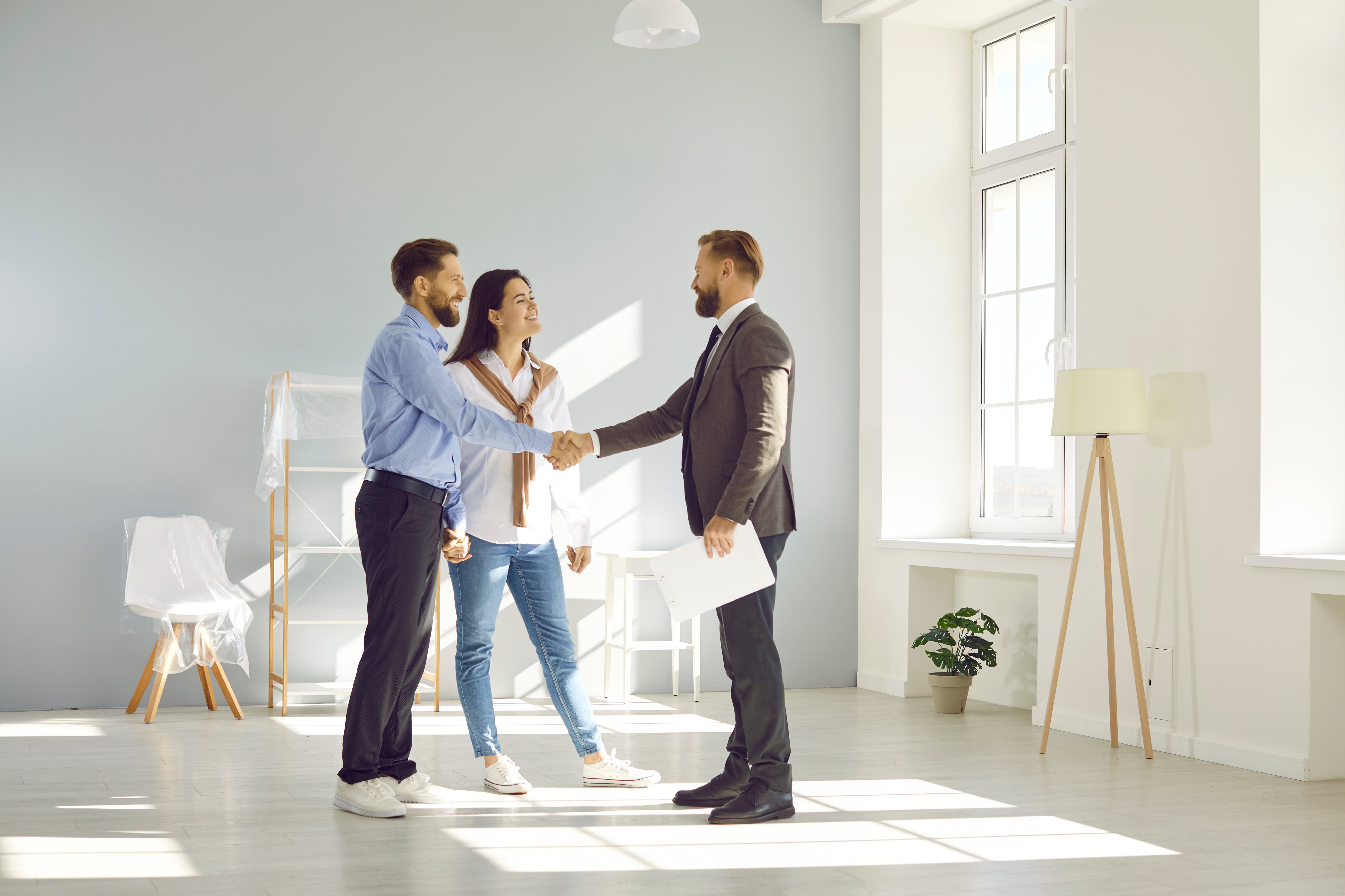 Property owners shaking hands with a new property manager in a bright, modern home, representing transition and hiring.
