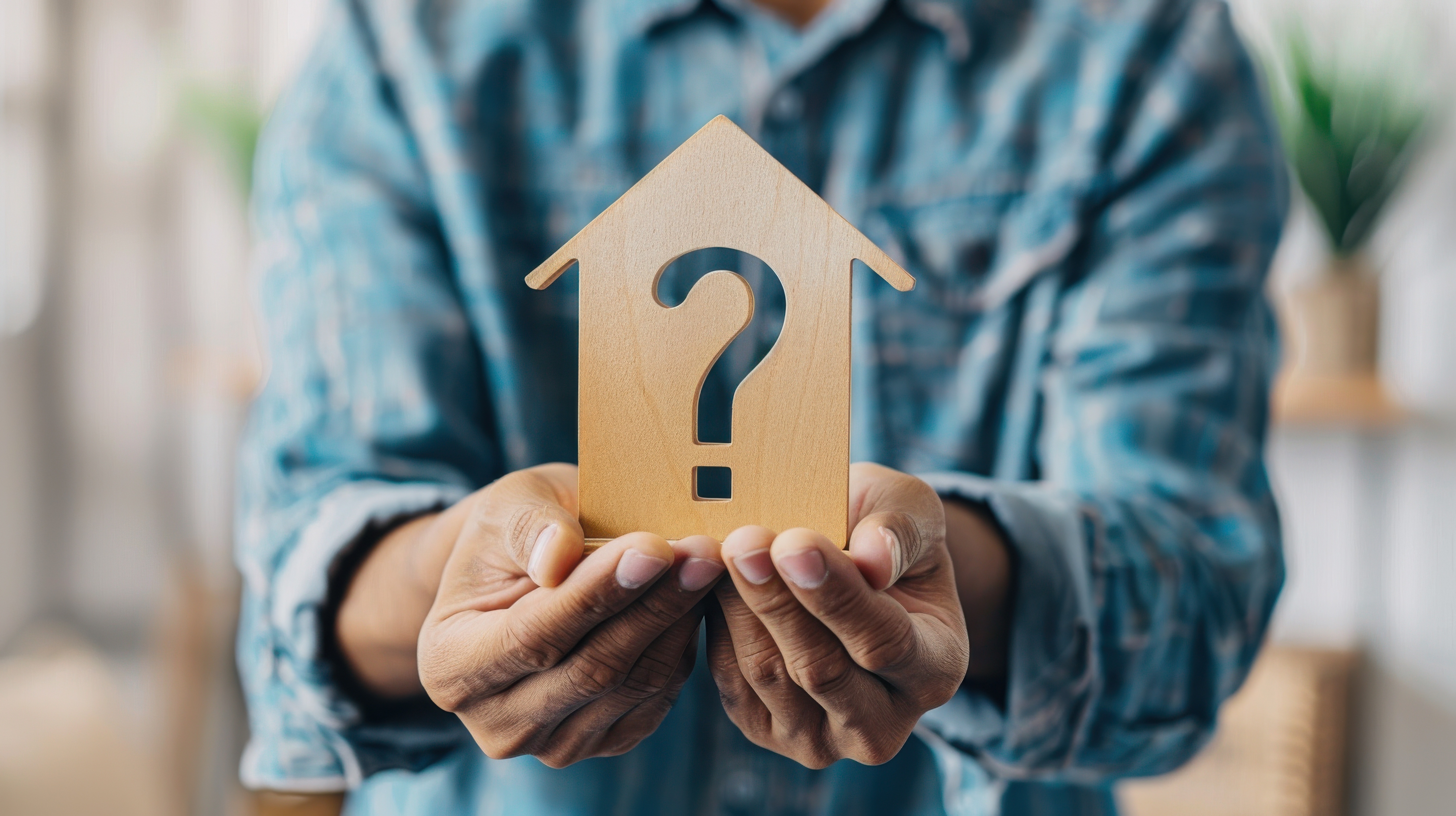 Person holding a wooden house cutout with a question mark in the center, symbolizing real estate investment decisions and common investor questions.