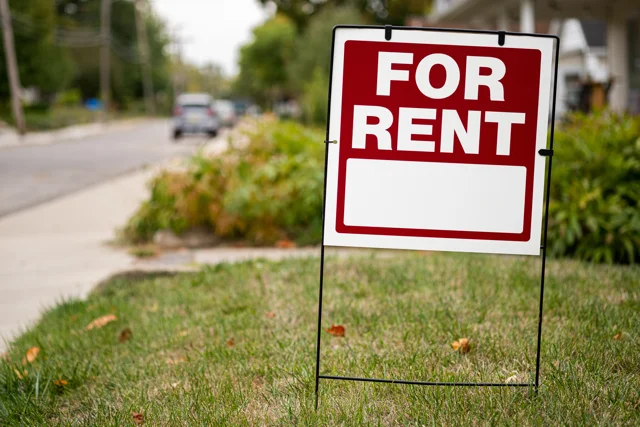 Red and white For Rent sign placed in front of a home available from a private landlord.