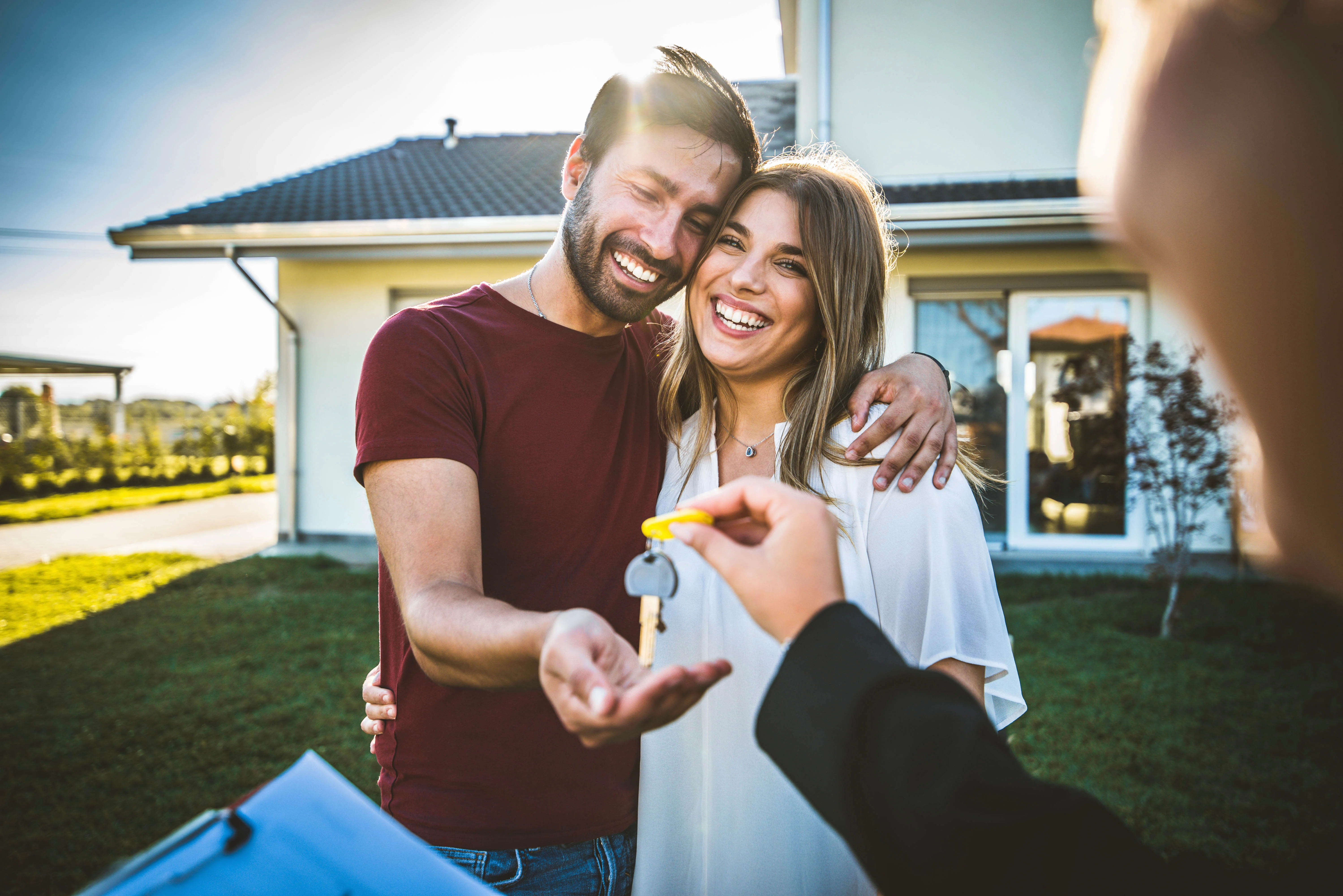 Smiling couple receiving keys from a private landlord in front of their new rental home
