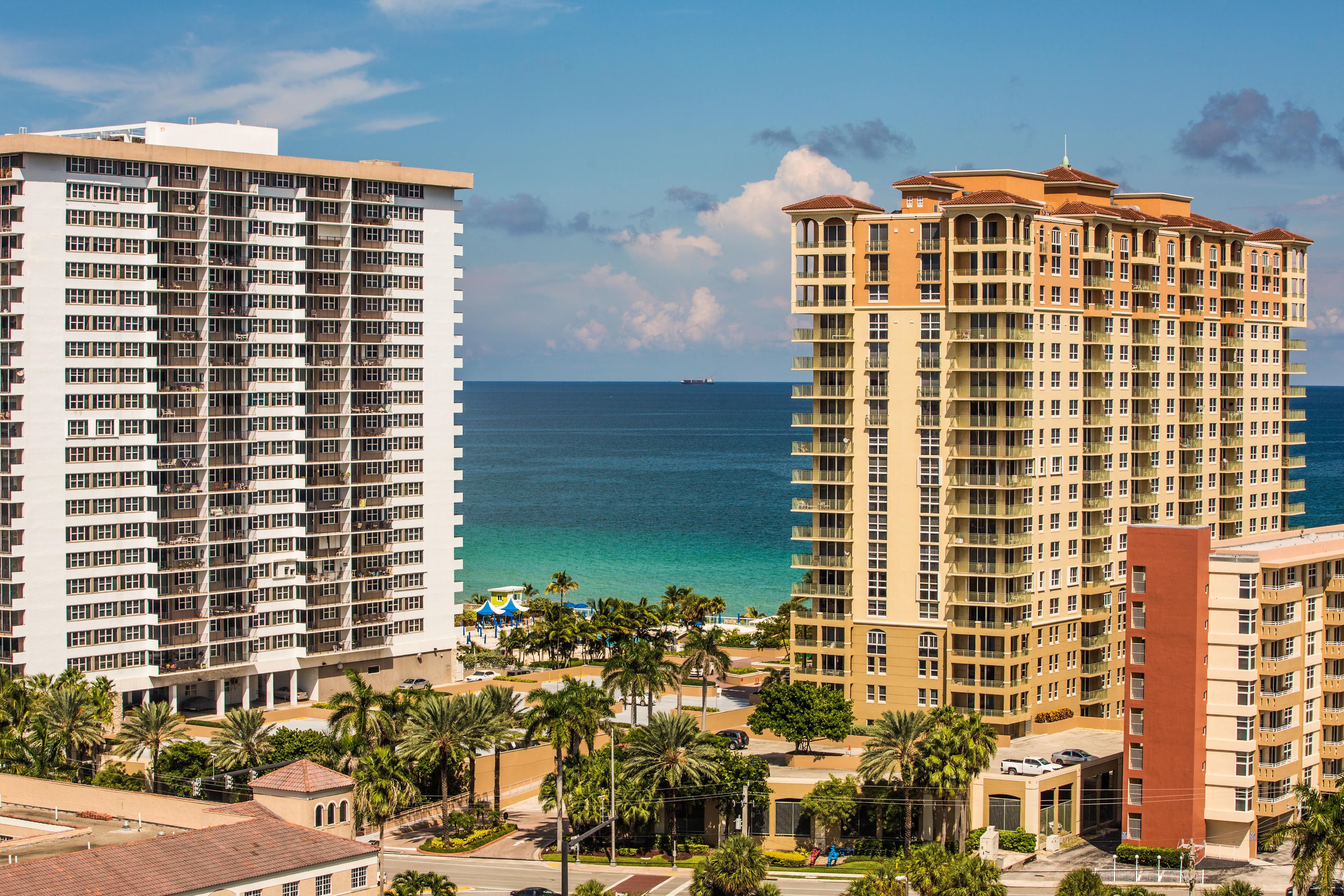High-rise beachfront condominiums along the Florida coast with palm trees and turquoise ocean in the background, representing residential communities affected by new HB 913 structural and financial regulations.