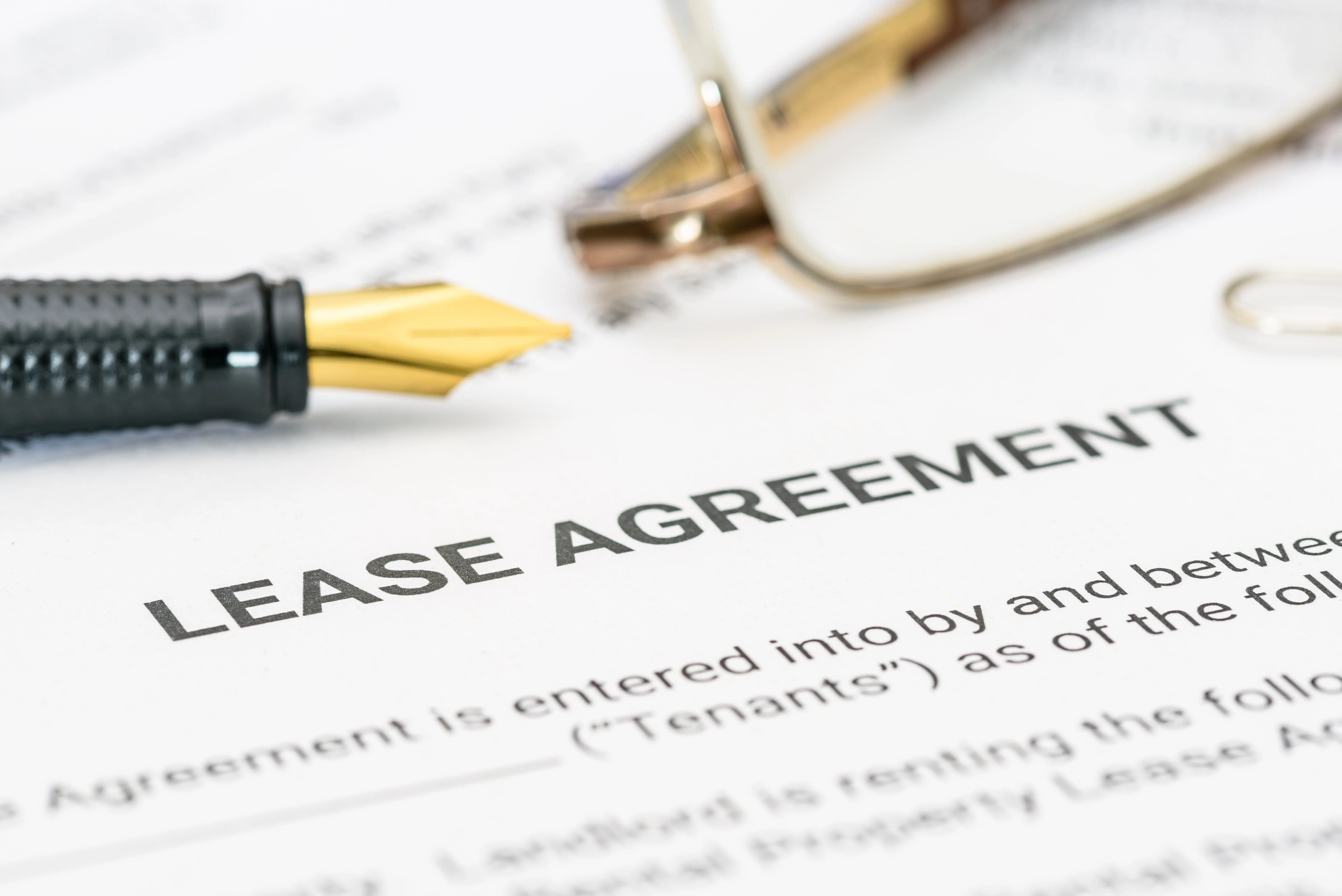 Close-up of a lease agreement with pen and glasses, illustrating rental contract signing between tenant and landlord.