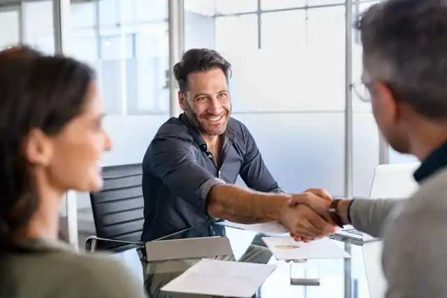 Smiling investor shaking hands with a business partner, symbolizing a successful deal in property management or real estate acquisition.