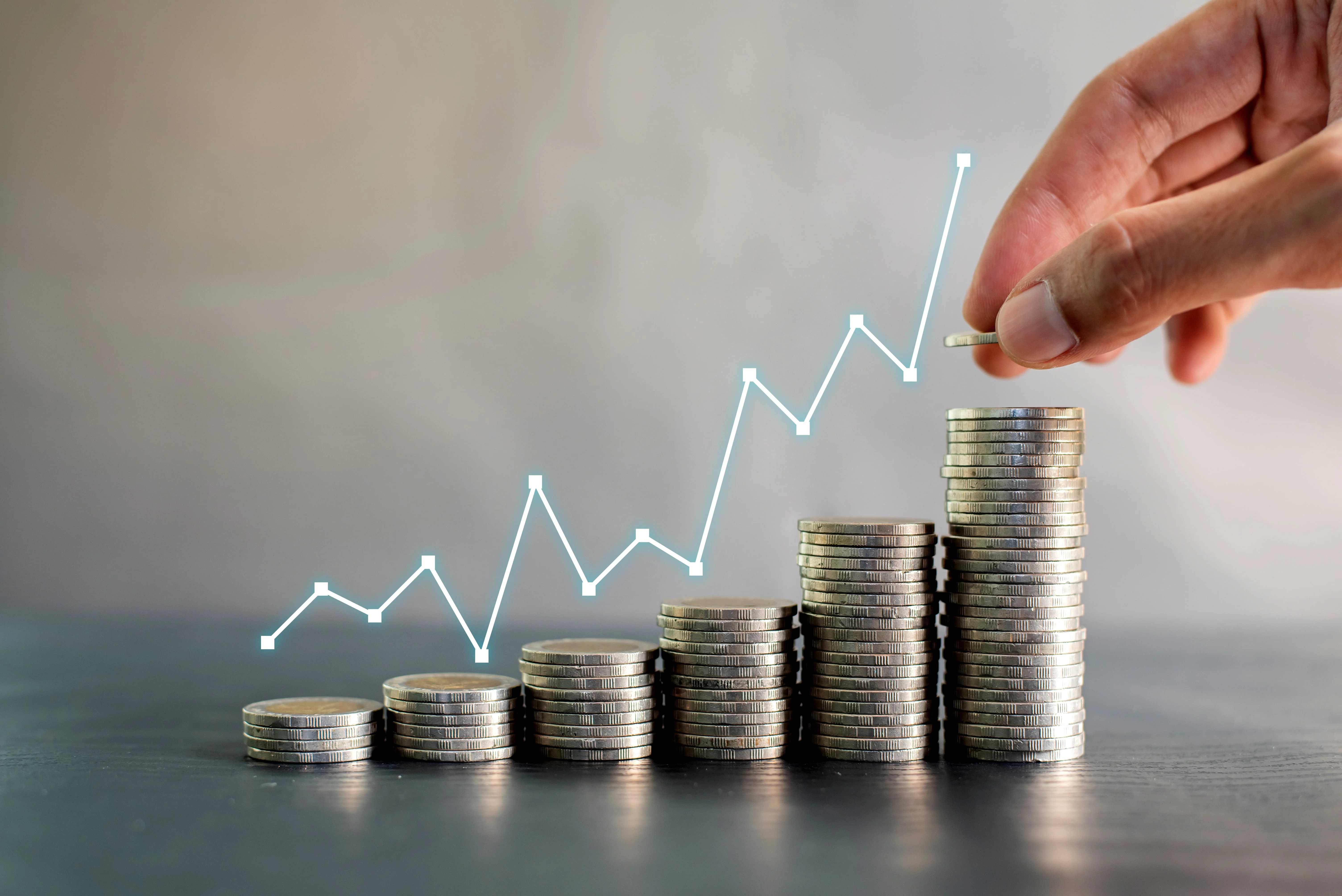 Hand stacking coins with upward graph overlay, symbolizing ROI growth in real estate investment and rental profitability.
