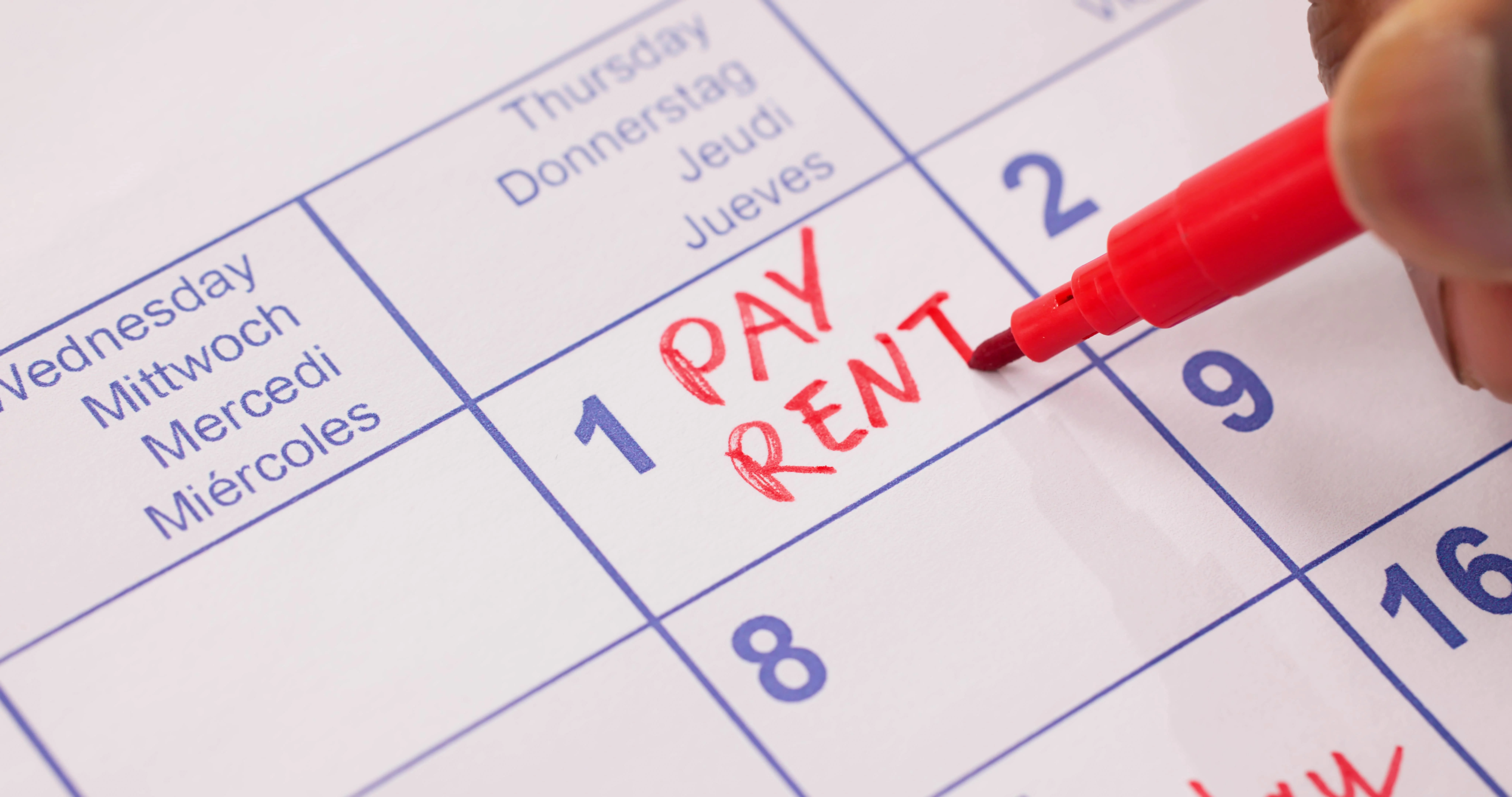 Hand writing “Pay Rent” on calendar with red marker, symbolizing rent payment schedule and tenant responsibility reminder.