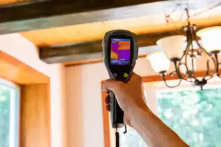 Inspector using a thermal imaging camera to detect moisture or heat loss during a rental property inspection.